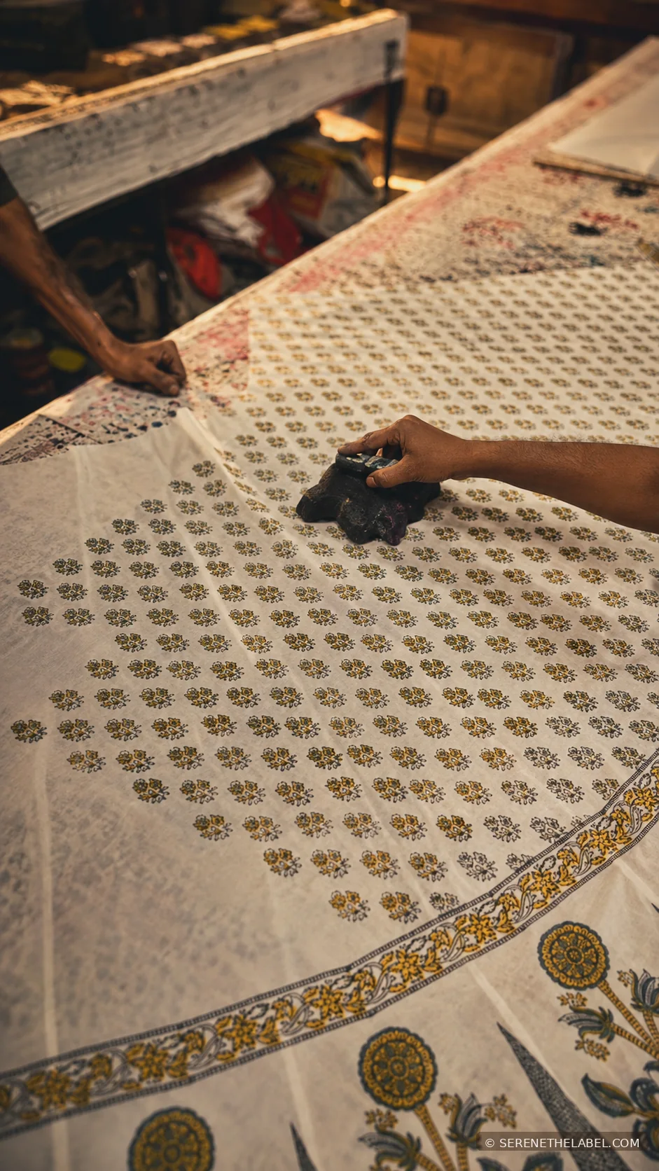 Artisan working by hand on printed fabric at a workshop table